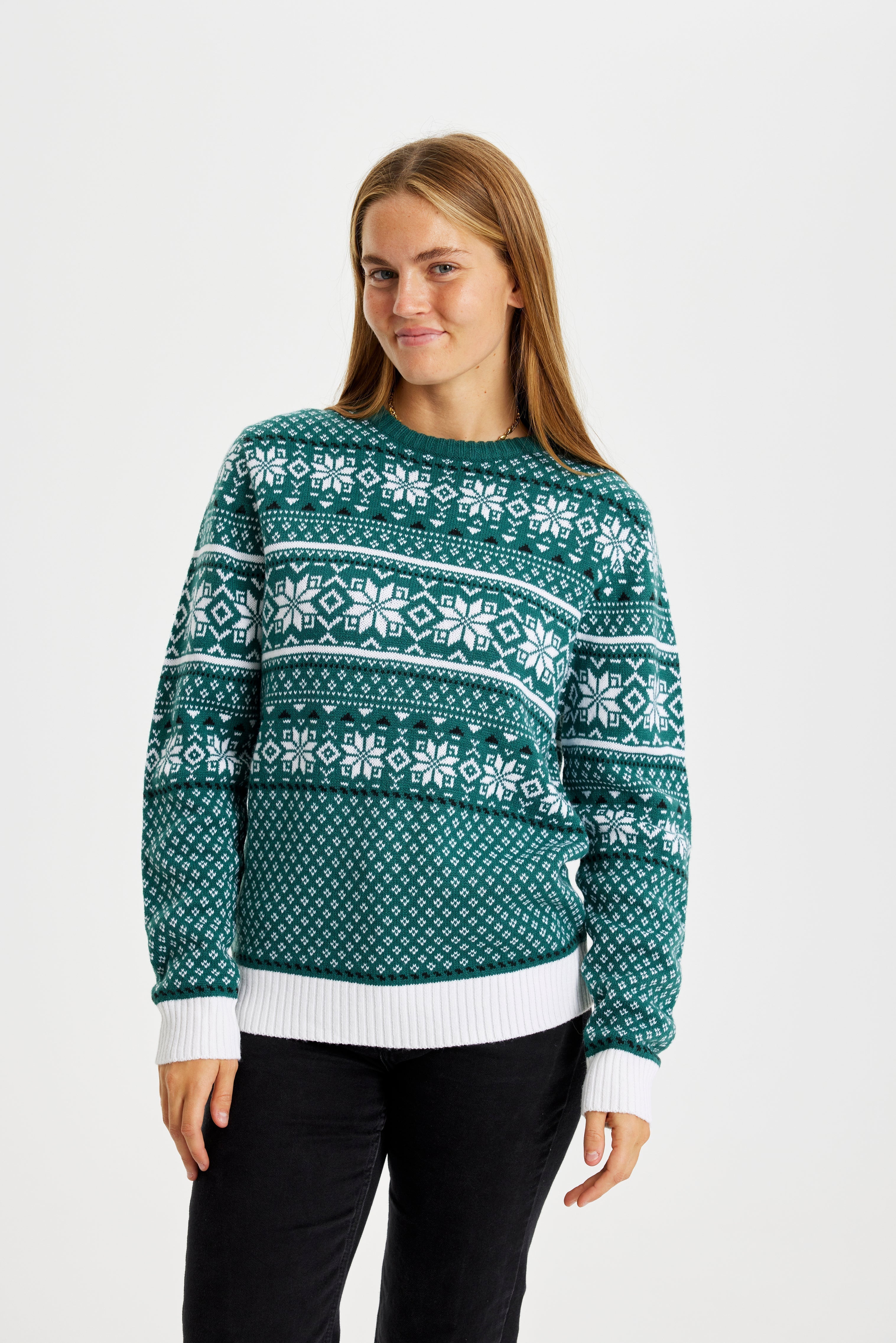 Une femme posant avec un pull de Noël vert avec des flocons de neige.